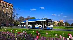 Modrý kloubový nízkopodlažní autobus Solaris Urbino III 18 s pohonem na CNG na MHD lince projíždějící po kruhovém objezdu na Hlavní třídě