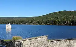 Vodní hladina vpředu snímku ohrazená kamenným bezpečnostním přelivem a v pozadí se vypíná vrchol Jizery.