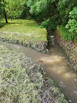Soutok potoka (vpravo nahoře) s výtokovou vodou (vlevo uprostřed) z dešťové usazovací nádrže (DUN) Jinonice těsně pod sypanou hrází suché retenční nádrže N4 Jinonice