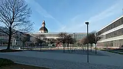 Barevná fotografie s pohledem na čtvercové nádvoří komplexu moderních budov, za nímž ční věž