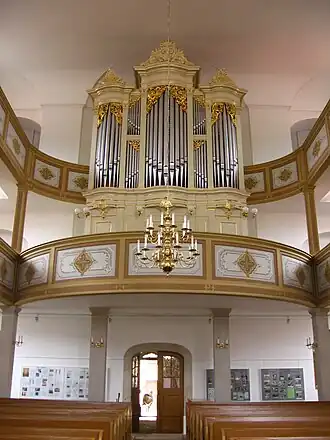 Uprostřed do hněda tónovaný zaoblený kůr, na něm jsou umístěné světlehnědé varhany se stříbrnými píšťalami, po stranách pokračují dvoupatrové galerie, pod kůrem je otevřený hlavní vchod a lavice v kostelní lodi