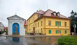 Kaple svatého Jana Nepomuckého na křižovatce uprostřed Třebívlic. Vpravo z boku budova zámku (dnes základní škola)