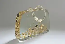 Ted Noten: Věno Agáty, svatební taška, dvojitý popruh z perel, akrylátové sklo, 1999. Na hranách světelné paprsky vytváří obraz vnitřního obsahu tašky, umístěno před nekonečným pozadím.