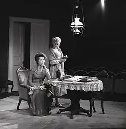 Frits Solvang: Scéna z inscenace Gengangere Henrika Ibsena z Národního divadla. Paní Alvingová sedí v křesle u stolu. Za ním je Regine Engstrand. Na stole je láhev šampaňského a mnoho knih. Premiéra: 4. října 1972. Pål Løkkeberg režie, Helen Brinchmann jako paní Alvingová, Frøydis Armand jako Regine Engstrand, Svein Sturla Hungnes jako Osvald, Frank robert jako Pastor Manders a Rolf Søder jako Snekker Engstrand. Oslo, asi 1972