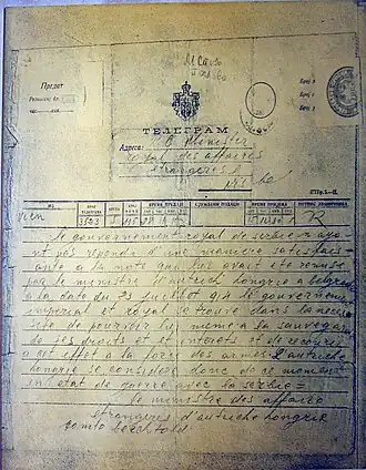 Fotografie ukazuje historický telegram, formulář vyplněný ručně psaným textem. Telegram má razítka a tištěné texty v cyrilici, zatímco adresa a text zprávy je v latince a psán francouzsky.