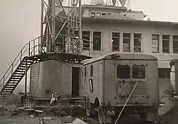 Zničená okna vysílacího sálu a maringotky po výbuchu, vlevo stožár vysílače.