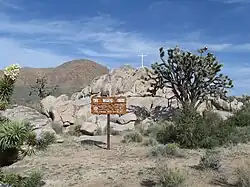 Rocky outcropping with a cross on top, tree and sign in foreground