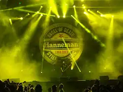 v pozadí za kapelou kruhové logo s nápisy Jeff Hanneman – Angel of Death Still Reigning, 1964–2013