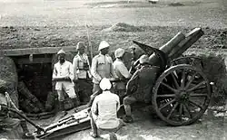 Sedm osmanských vojáků obsluhujících kanón umístěný v zákopů v pouštní krajině.