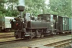 Úzkorozchodná parní lokomotiva U 37.002 stojí na kolejích v čele vlaku.