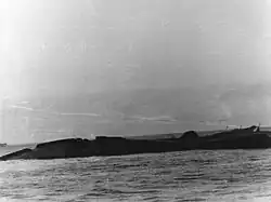 Černobílá fotografie převrácené lodi, nad hladinou zůstává pouze spodek.