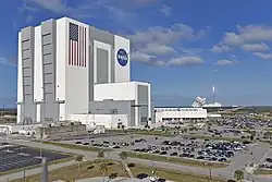 Pohled na VAB, v pozadí letící raketa Falcon Heavy z LC-39A