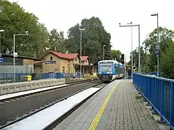 Celkový pohled na nádražní budovu s osobním vlakem z Jablonce, který přijíždí na zastávku Vesec u Liberce a pokračuje do Liberce