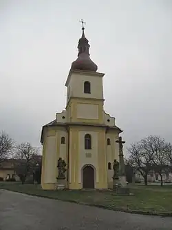 Trojúhelníková náves s kostelem svatého Matouše z roku 1867. Před ním barokní sochy a krucifix z 18. století.