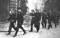 Varšavské povstání, Shromáždění čety I / 1147 na dvoře mezi domy 2/4 náměstí Dąbrowskiego a Mazowiecka 11. Před frontou (s raněnou paží) velitel čety 2. por. Leopold Kumant "Riga". Četa I / 1147 za povstání, disponibilní jednotka štábu okresu Śródmieście, patřící rotě kpt. Bolesław Kontryma „Żmudzina“, pocházel z podzemní bojové diverzní jednotky (ODB 3) okresu Śródmieście, které velel poručík Kazimierz Pogorzelski „Rygla“, který zemřel 2. srpna na náměstí Małachowského