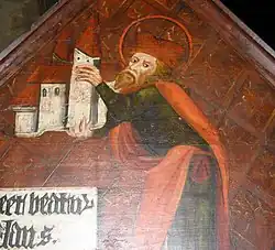 Obraz muže s rudým plnovousem na červeném pozadí. V obou rukách drží kostel