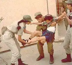 Tři vojáci drží vzpouzející se dítě s kipou