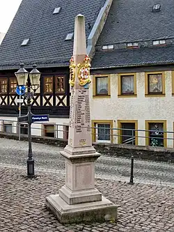 Poštovní milník s historickými měšťanskými domy v pozadí